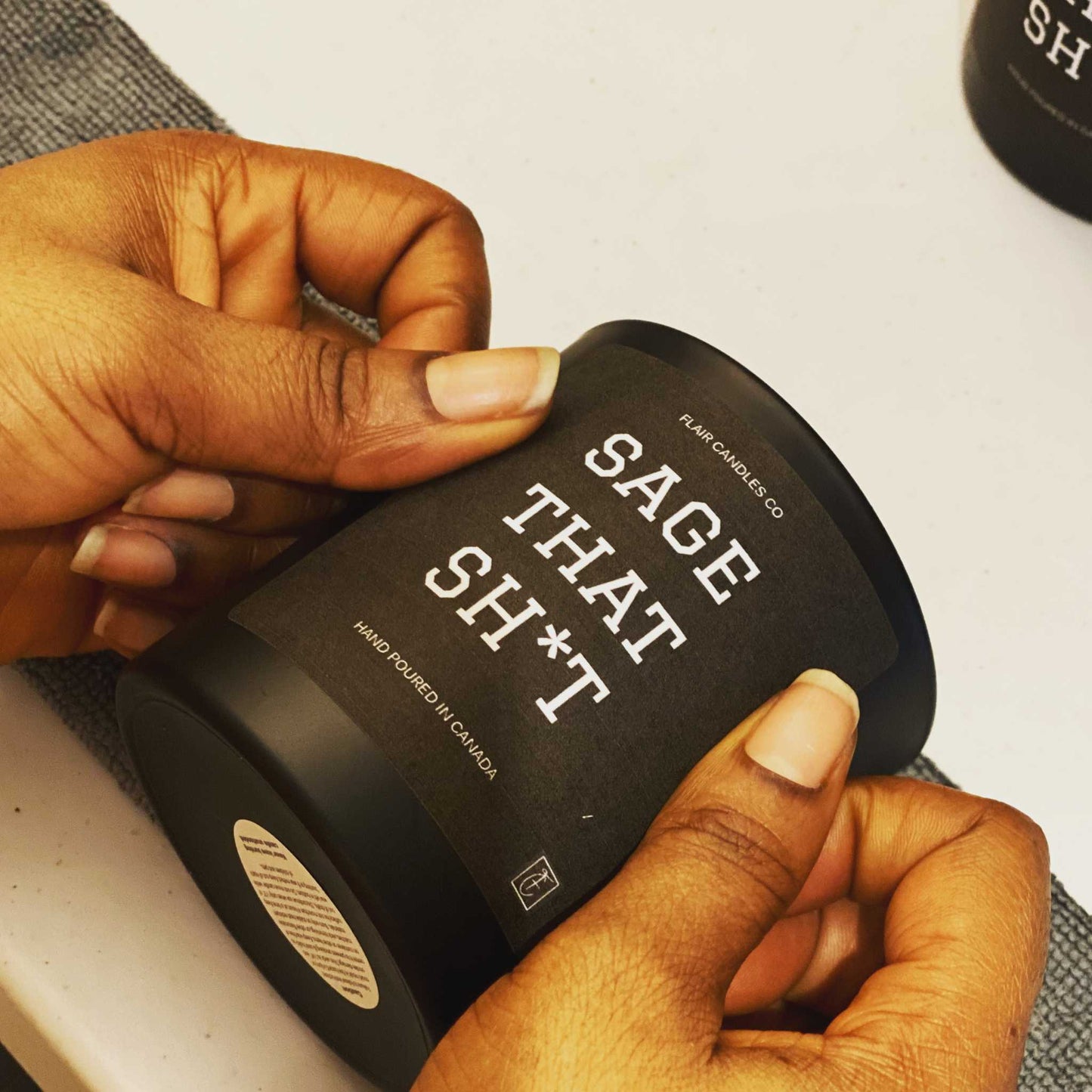 Hand holding Sage That Sh*t soy wax candle with sage, leather, mahogany, and teakwood scent in black matte jar