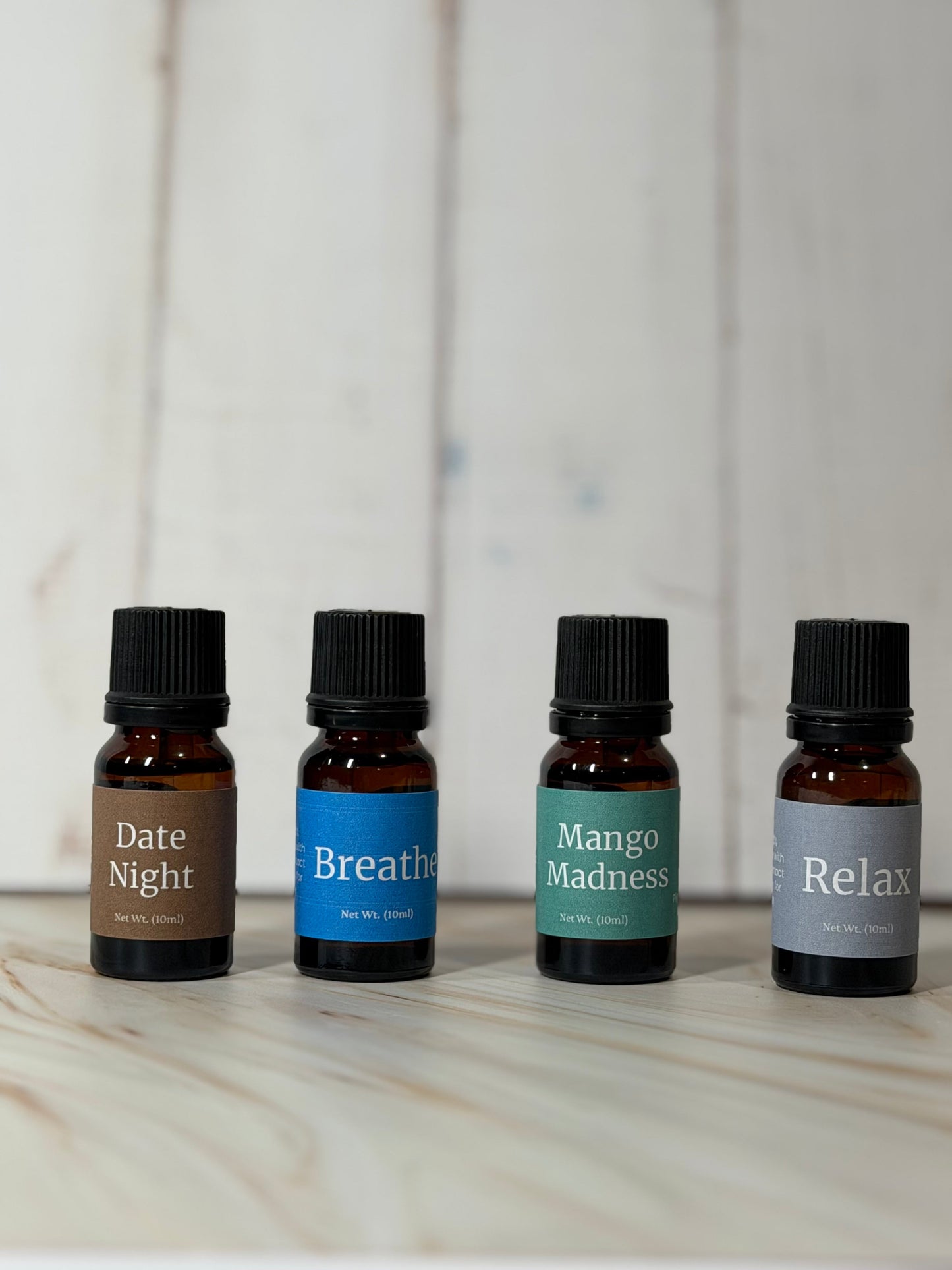 Essential oil blend diffuser bottles labeled Date Night, Breathe, Mango Madness, and Relax on wooden surface