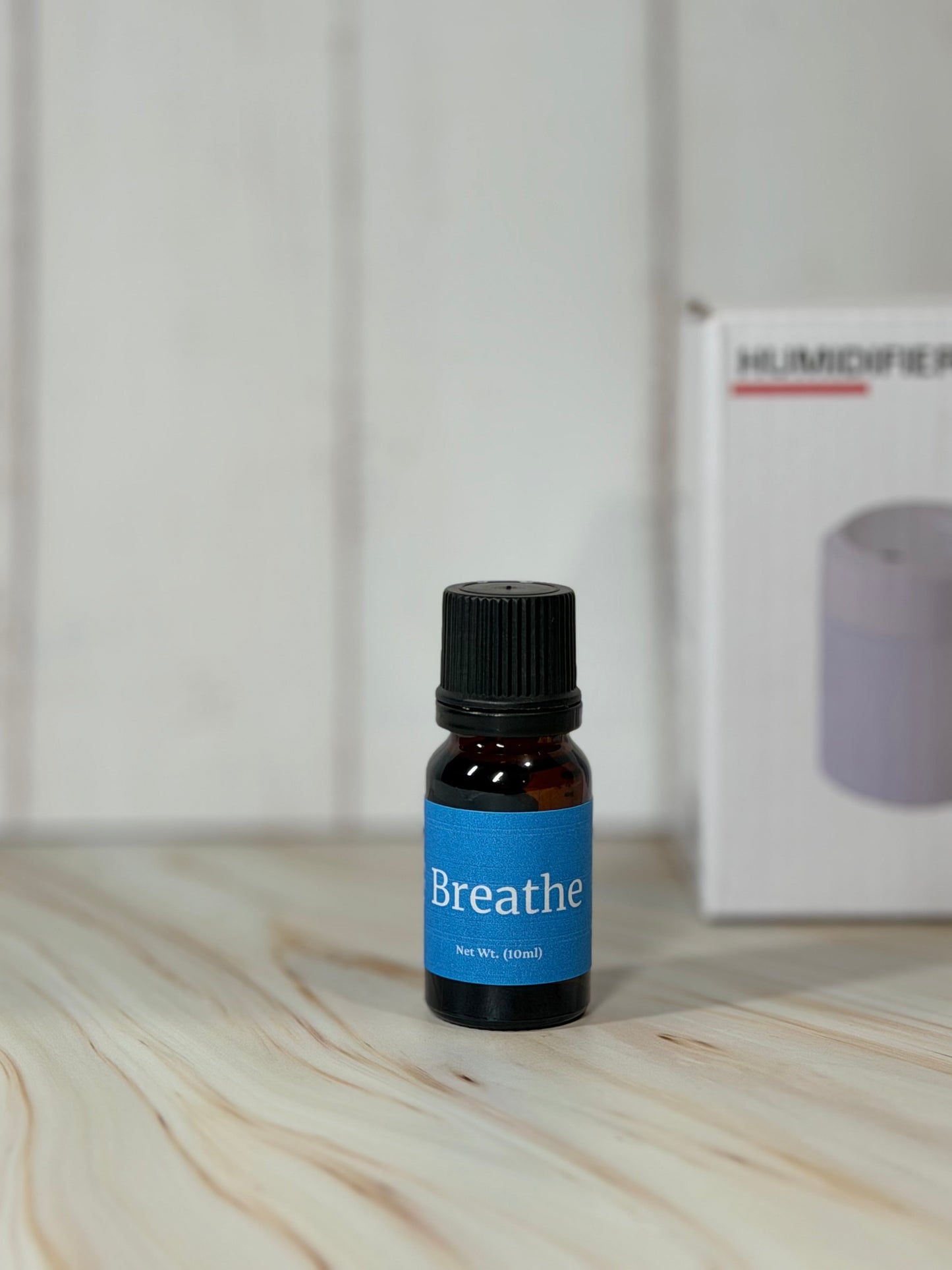 Essential oil blend bottle labeled Breathe with diffuser in background on wooden surface
