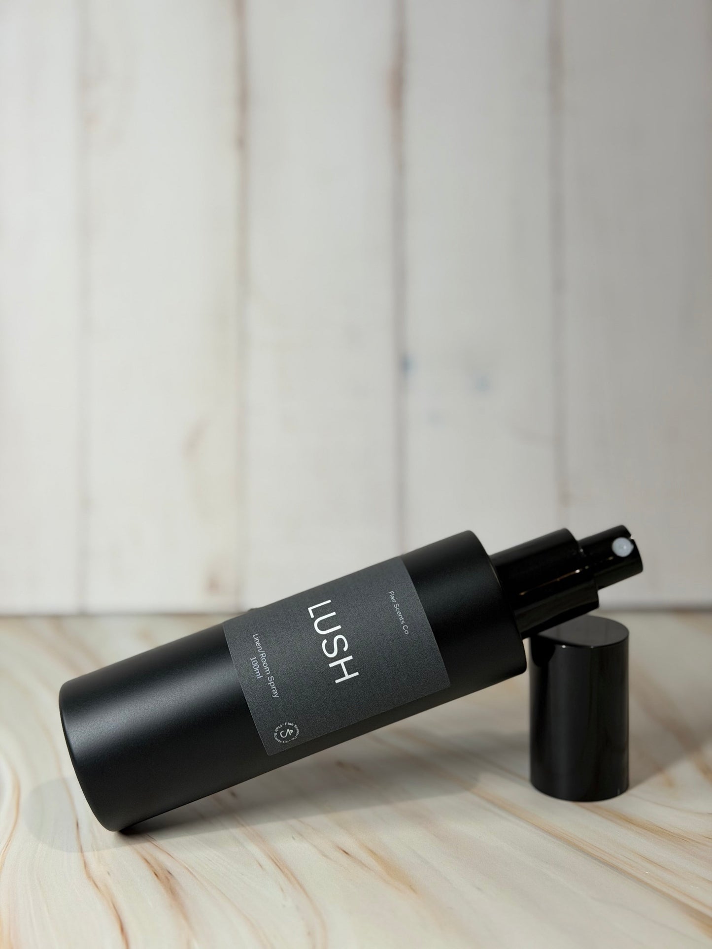 Black Lush room spray bottle with enchanting scent of patchouli, lavender, and rose petals on wooden surface