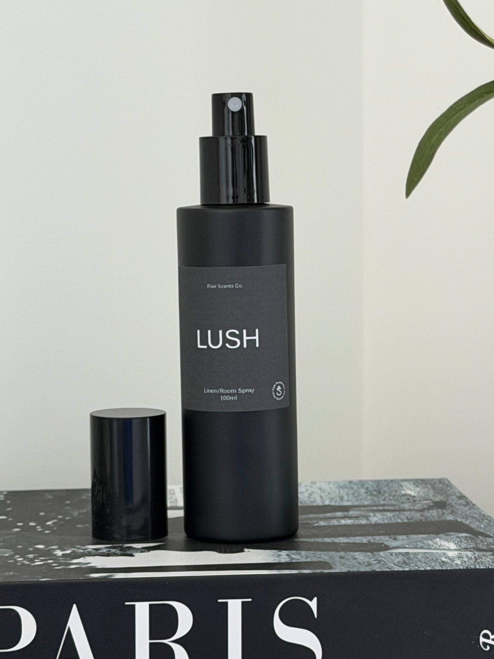 Black 100ml Lush room spray bottle with enchanting scent of patchouli, lavender, and rose petals on a book background