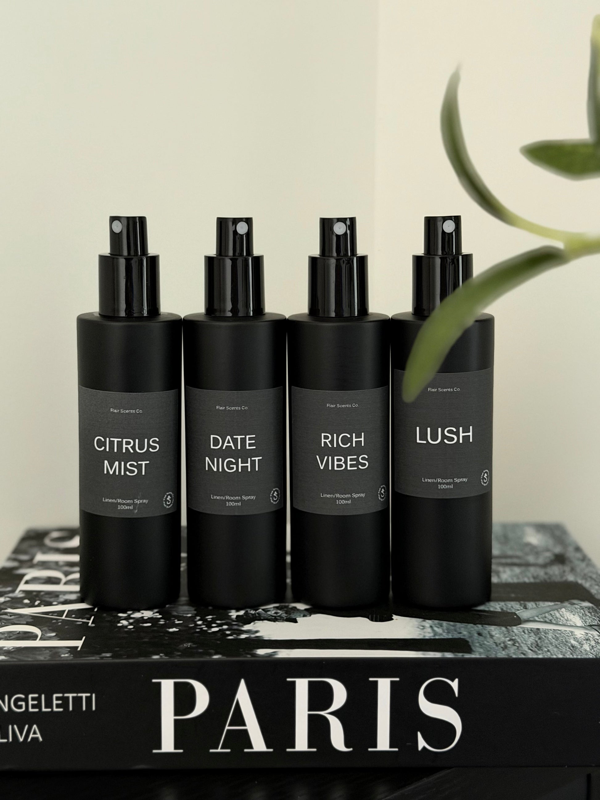 Room/Linen Spray bundle with four black bottles featuring Citrus Mist, Date Night, Rich Vibes, and Lush scents on a Paris book