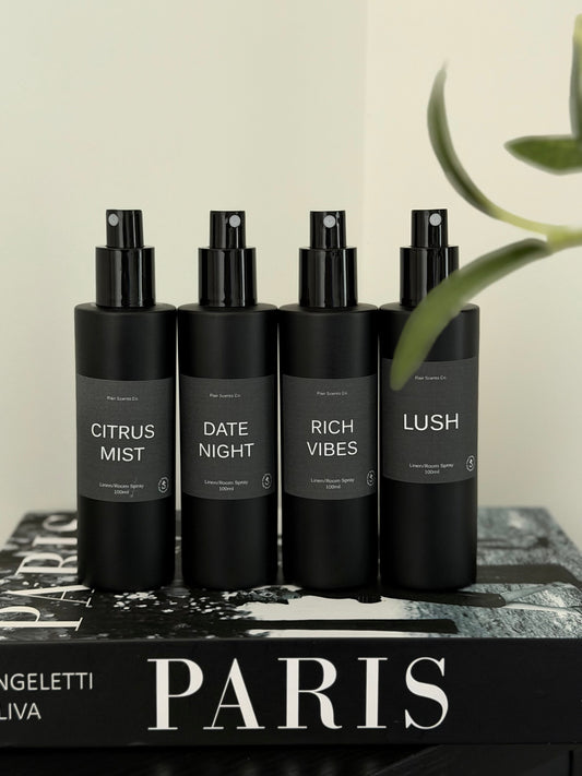 Room/Linen Spray bundle with four black bottles featuring Citrus Mist, Date Night, Rich Vibes, and Lush scents on a Paris book