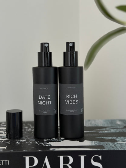 Room/Linen Spray bundle with Date Night and Rich Vibes scents in black bottles on book.
