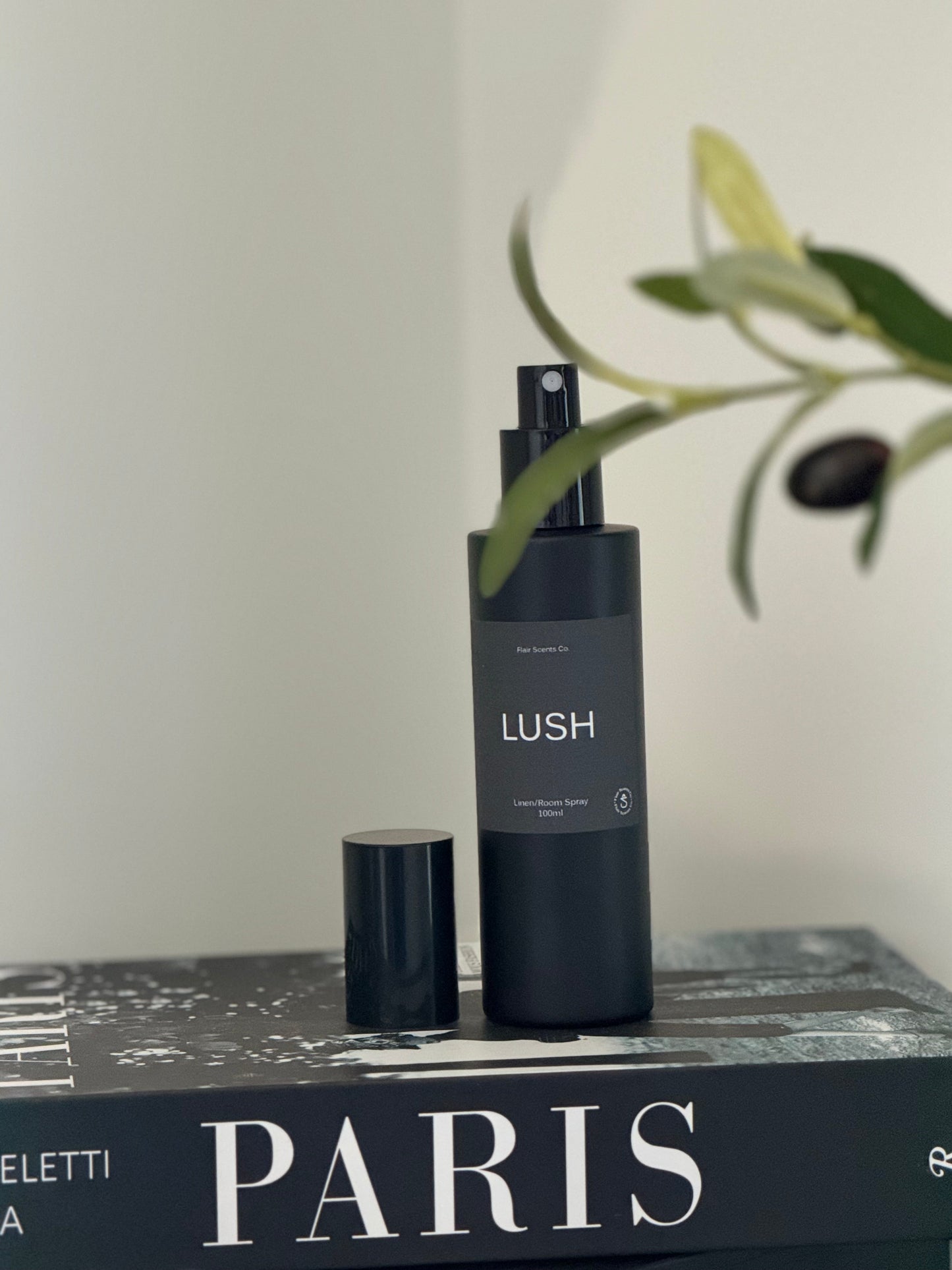 Lush room spray bottle with enchanting scent of patchouli, lavender, and rose petals on a book titled Paris