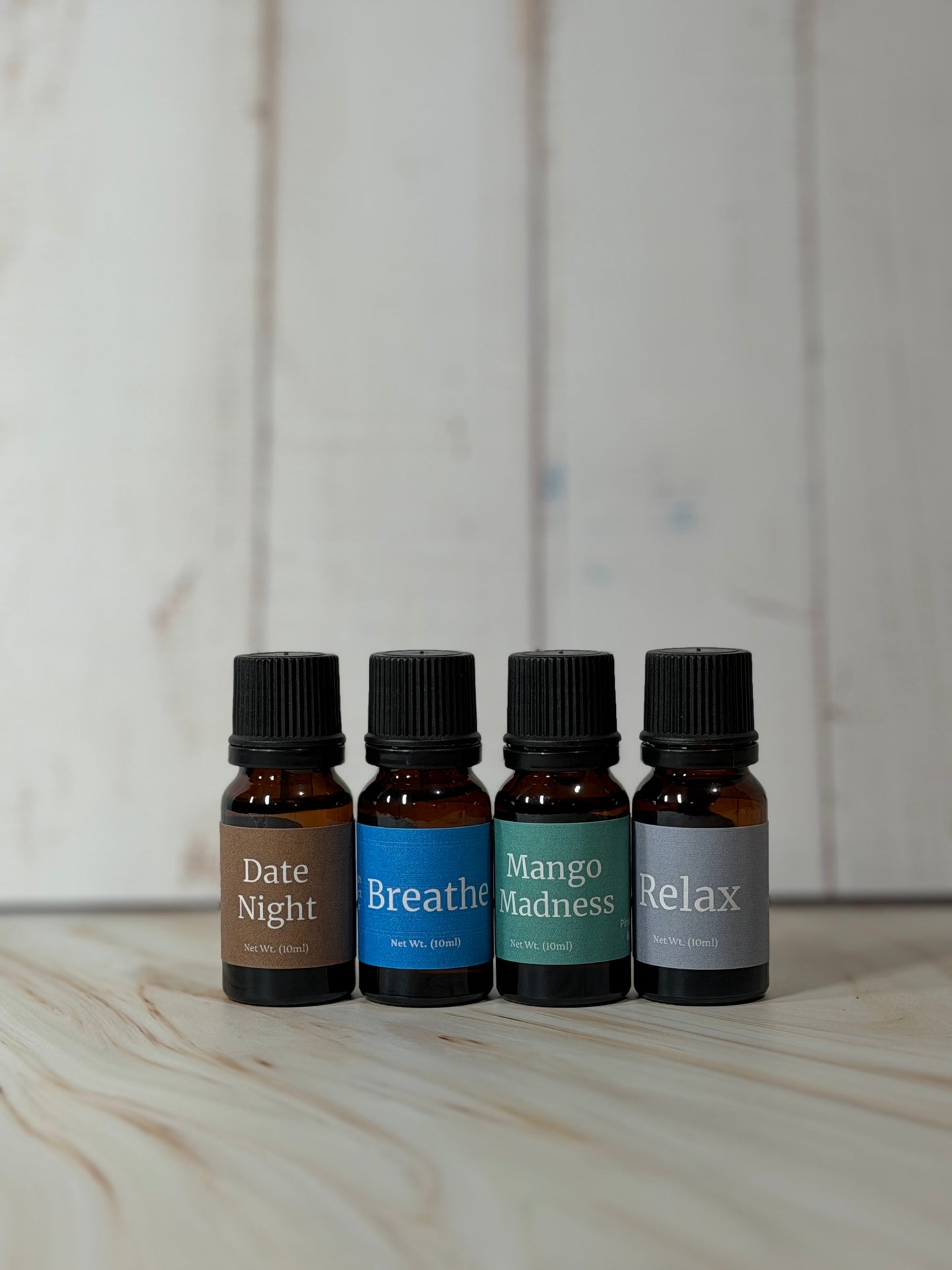 Essential Oil Blend bottles with Relax, Breathe, Date Night, and Mango Madness labels on wooden surface