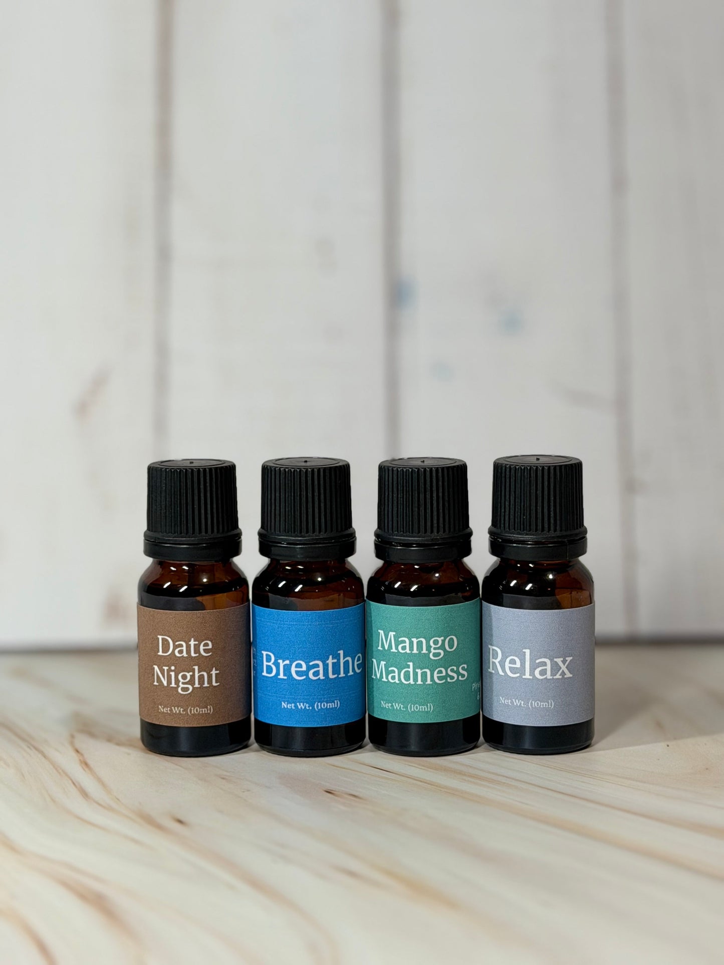Four essential oil blend diffuser bottles labeled Date Night, Breathe, Mango Madness, and Relax on wooden surface
