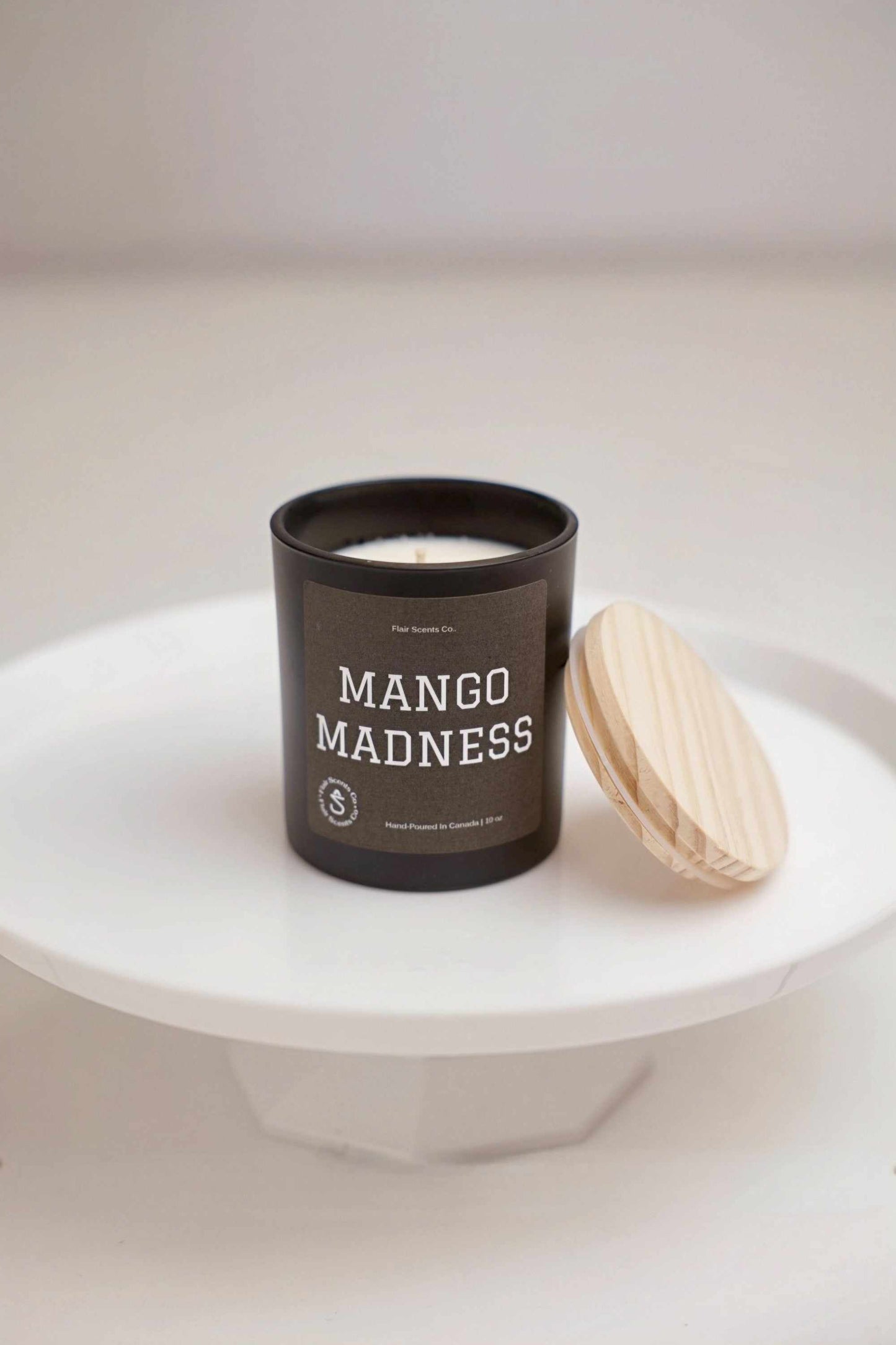 Mango Madness tropical dessert candle in black jar with wooden lid on white stand