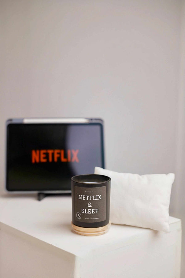 Netflix and Sleep scented candle with 100% organic soy wax, eucalyptus, peppermint, and lime notes next to a pillow and tablet displaying Netflix logo