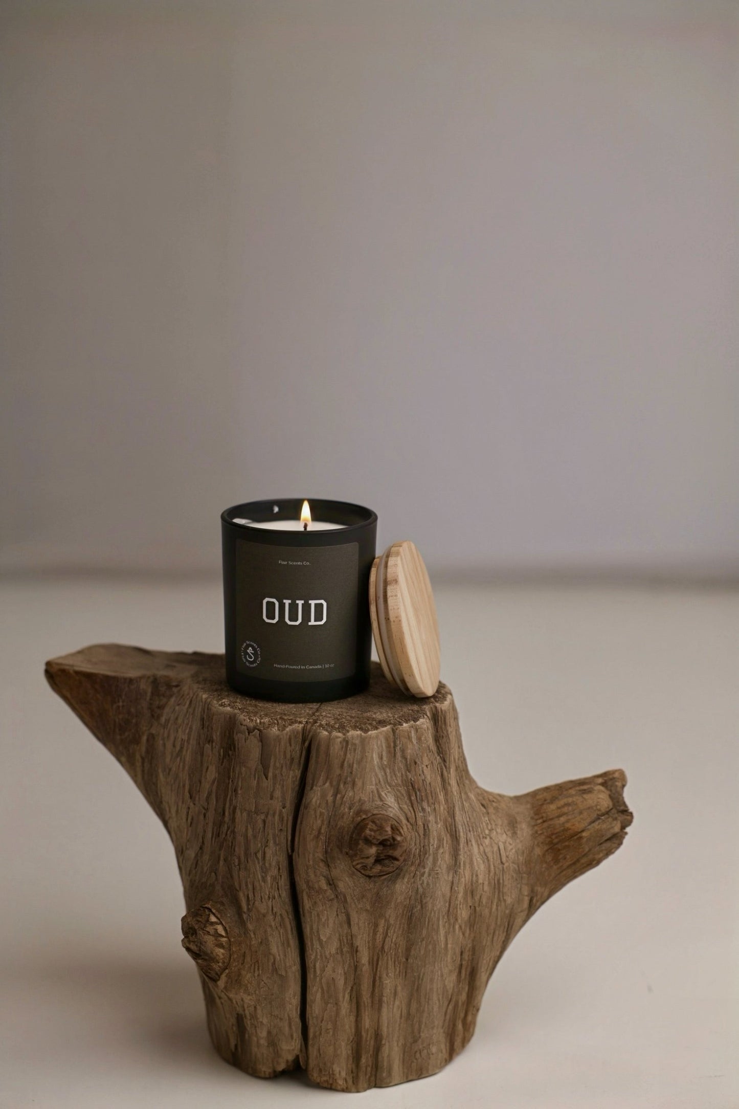 Black candle labeled Oud with wooden lid on rustic tree stump, featuring Moroccan oud scent