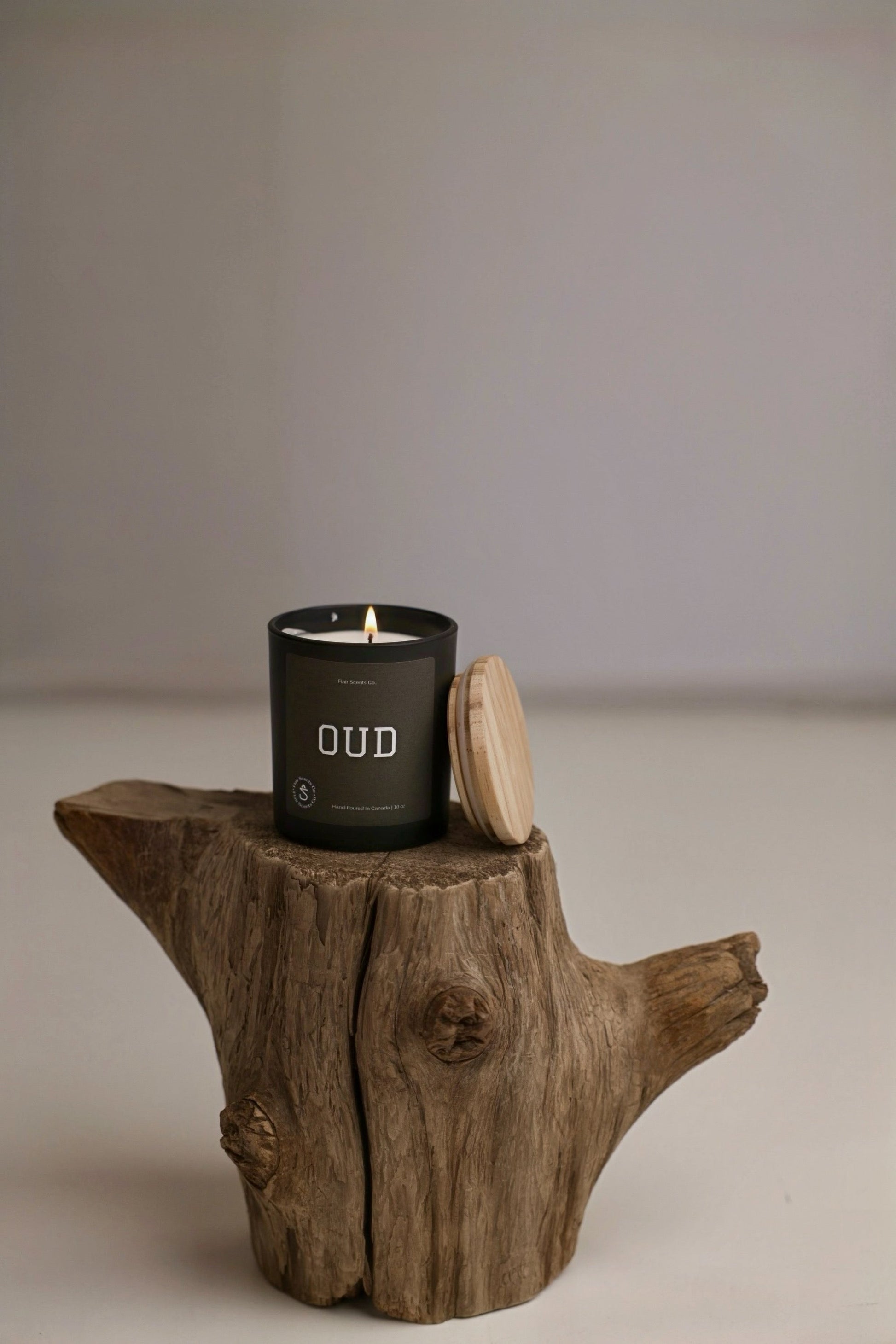 Black candle labeled Oud with wooden lid on rustic tree stump, featuring Moroccan oud scent