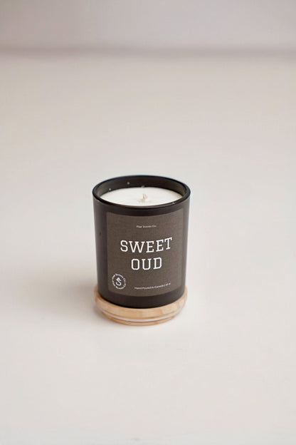 Sweet Oud organic soy wax candle with Moroccan oud, sweet patchouli, sandalwood scent in black holder on wooden base
