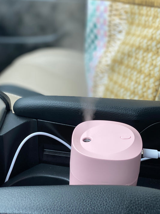 Mini Ultrasonic Scent Buster pink humidifier emitting mist in a car cup holder with USB power connection